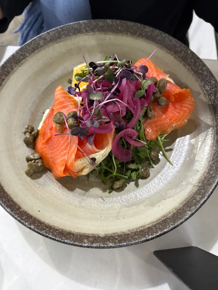Smoked salmon with capers, pickled red onion, rocket and microgreens in a stoneware bowl.